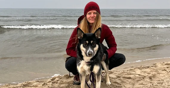 Foto einer jungen Frau, am Strand hockend mit ihrem Hund