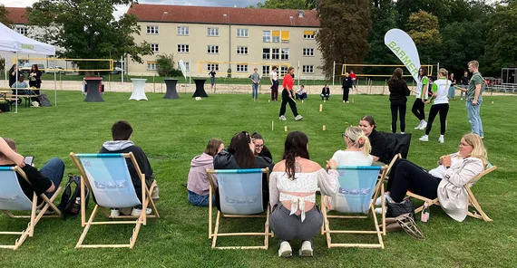 Auszubildende und Mitarbeitende der BARMER sowie der Universität Potsdam verbringen Zeit auf einer Wiese. Manche in Liegestühlen, manche beim Wikingerschach spielen.