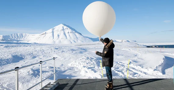 Markus Rex auf einer Expedition mit großem Wetterballon in der Hand. Im Hintergrund Schnee und Eis.