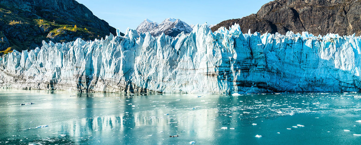 A glacier front that extends to the water in the foreground. Mountain formations in the background. - 