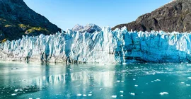 A glacier front that extends to the water in the foreground. Mountain formations in the background.