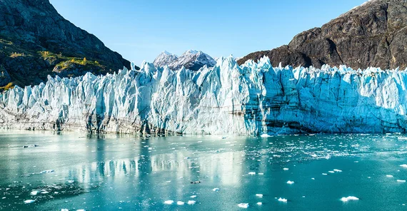 A glacier front that extends to the water in the foreground. Mountain formations in the background.
