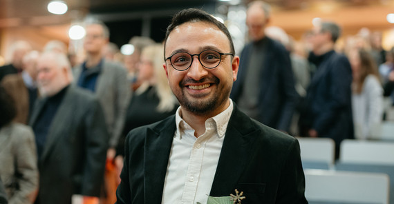 Ein Mann steht mit Blumenstrauß und Auszeichnung in einem Hörsaal