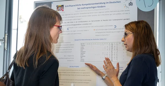 Zwei Frauen stehen vor einer Pinnwand und sprechen miteinander