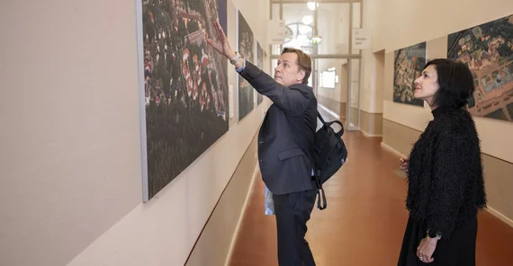 Zwei Menschen stehen vor einem Foto, ein Mann zeigt der zweiten Person, einer Frau, etwas auf einem Bild