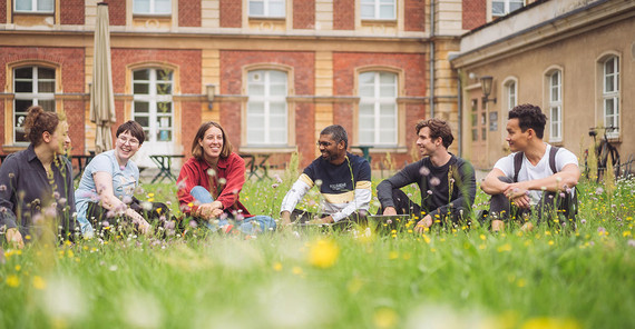 Studierende auf einer Wiese sitzend vor historischen Gebäuden der Uni Potsdam.