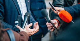 Auf dem Bild sind Mikrofone vor einer Person im Anzug zu sehen.