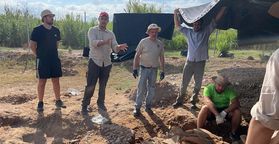 Der Museumsdirektor berichtet an der Ausgrabungsstätte. Mindestens fünf Personen hören ihm zu.
