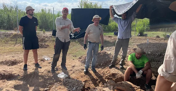 Der Museumsdirektor berichtet an der Ausgrabungsstätte. Mindestens fünf Personen hören ihm zu.