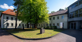 Das Deutsche Institut für Ernährungsforschung (DIfE) in Rehbrücke. Außenansicht des Gebäudes. Im Vordergrund ist eine Grünfläche mit großem Laubbaum zu erkennen.