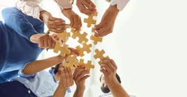 Mehrere Personen halten Puzzleteile aneinander. Froschperspektive.