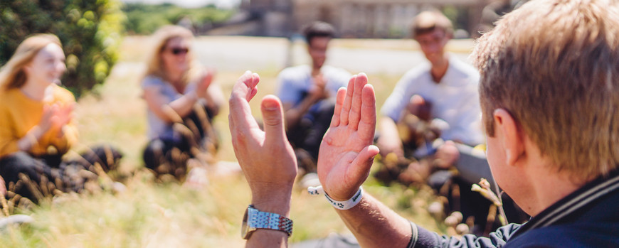 Studierende im Sitzkreis auf der Wiese vor dem Neuen Palais