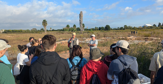 Gruppe von Menschen stehen vor einer Ausgrabungsstätte, während ihnen ein Mann etwas erklärt