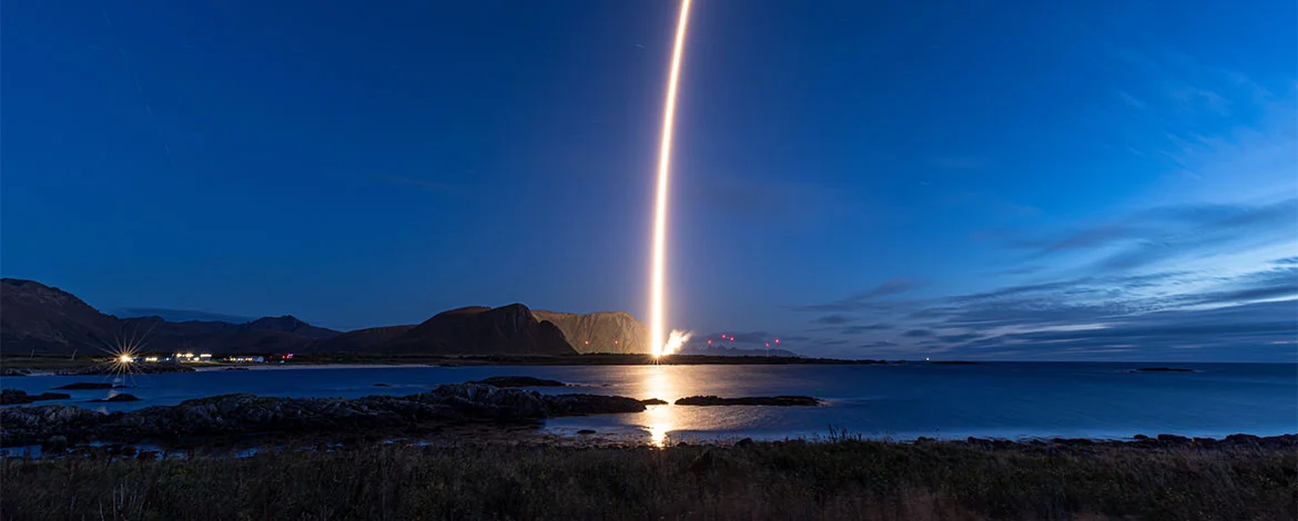 Illuminated rocket launch from a distance in stark contrast to dark night sky. - 