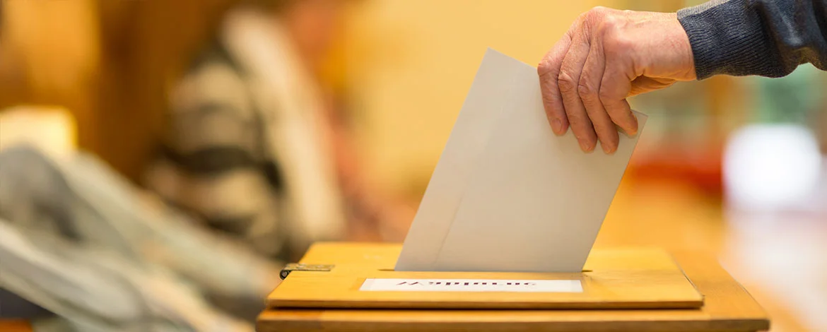 Eine Hand wirft einen Wahlzettel in eine Wahlurne. - 