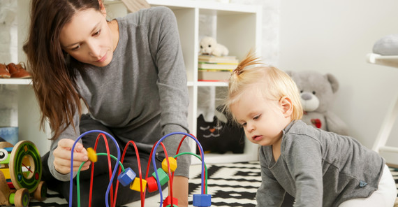 Eine Mutter sitzt mit einem Kleinkind und einem Spielzeug auf dem Boden. Das Foto ist von AdobeStock/triocean.