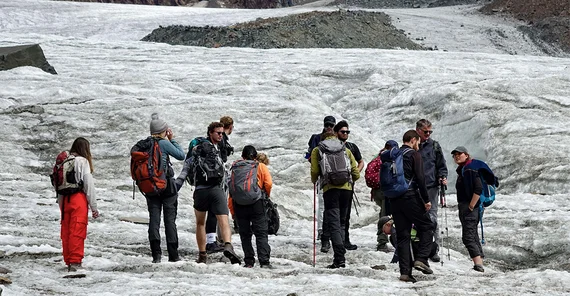Eine Gruppe von ca. 10 Menschen an einem Berg stehend in Outdoor-Kleidung.