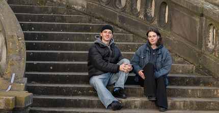 Two people are sitting on a staircase and looking at the camera.