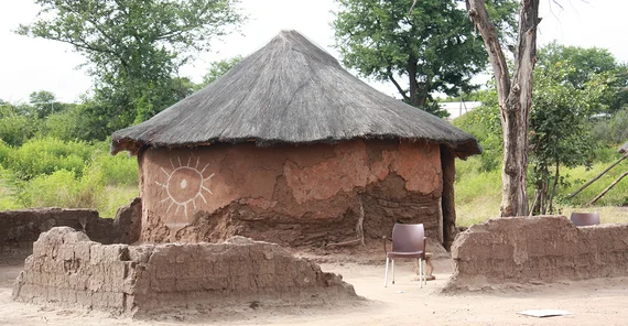 Afrikanische Lehmhütte, an einer Mauer mit Schäden, die durch einen Elefanten entstanden.