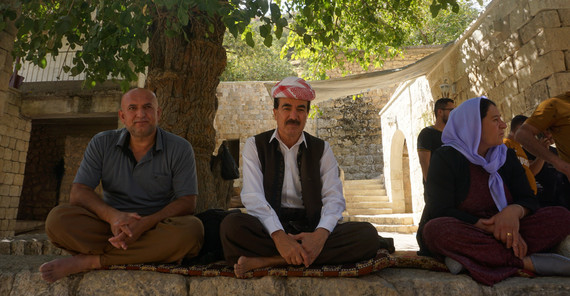 Zu Besuch in Lalish, dem Ort, an dem laut jesidischem Glauben der Ursprung der Schöpfung liegt. | Foto: Valentina Meyer-Oldenburg Das Bild zeigt im Vordergrund drei Personen die auf einer Mauer sitzen.