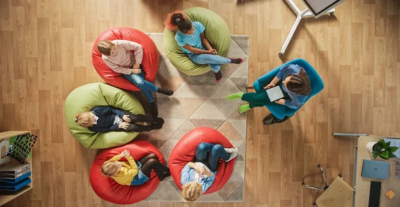 Ein Stuhlkreis aus der Vogelperspektive mit Kindern und einer erwachsenen Person.