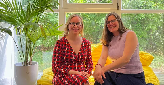 Zwei Frauen sitzen auf einer Fensterbank und schauen in die Kamera