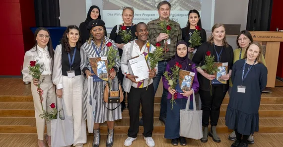 Es ist ein Gruppenfoto. Zwölf Absolventinnen und Absolventen des Refugee Teachers Program der Universität Potsdam halten ihre Abschlusszertifikate.