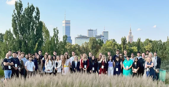 Student representatives gathered on a lawn for a group photo. The Warsaw skyline can be seen in the background.
