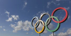 Das Bild zeigt die Olymischen Ringe vor blauen Himmel. Das Foto ist von AdobeStock/ink drop.
