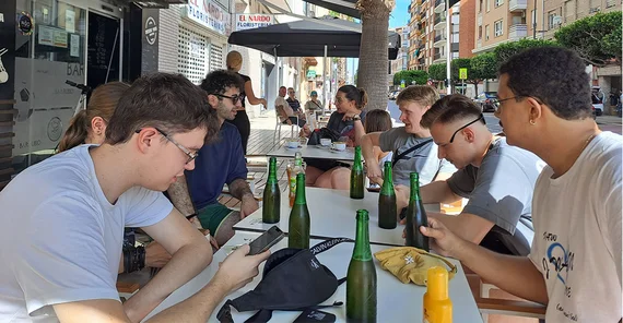 Die Studierenden sitzen an einem Tisch in einem Straßencafé und genießen kühle Getränke.