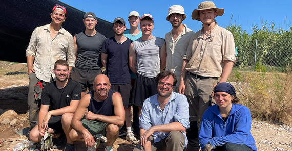 Gruppenbild der Angehörigen der Universität Potsdam am Grabungsort. Es sind elf Personen auf dem Bild zu erkennen. Sie alle tragen Kleidung, die praktisch und funktional ist beim körperlichen Arbeiten in Sand und Sonne.