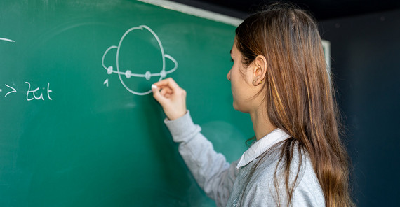 Heute studiert Weiß Physik an der Uni Potsdam. Später möchte sie als Wissenschaftlerin arbeiten. Anna-Maria Weiß steht an einer Tafel.