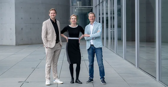 (v.l.n.r.): Dr. Kilian Hampel, Prof. Dr. Nina Kolleck, Simon Schnetzer posierend in Vollansicht vor grauem moderenen Gebäude.