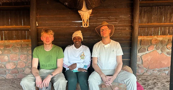 drei Menschen sitzen in einer Holzhütte unter einem Tierschädel
