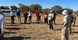 Menschen stehen auf einer Rasenfläche in Namibia, eine von ihnen erzählt