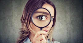 Portrait of a young woman holding up a magnifying glass to her eye