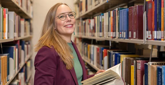 Porträt einer Frau, die im Gang einer Bibliothek steht