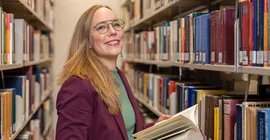 Porträt einer Frau, die im Gang einer Bibliothek steht