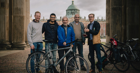 Gruppe von Menschen steht zwischen Säulen, einer übergibt ihnen einen Pokal